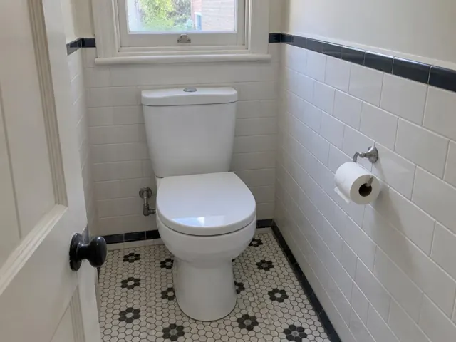 Clean white toilet in a tiled bathroom with a window and patterned floor in Double Bay