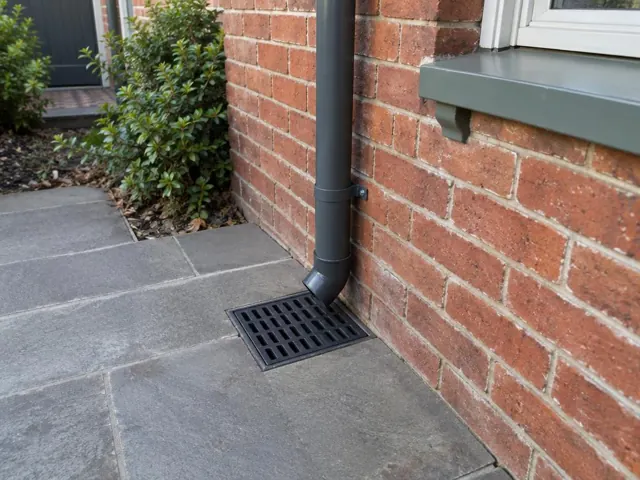Stormwater grate beside a brick wall with downpipe and dry paved path in Woollahra